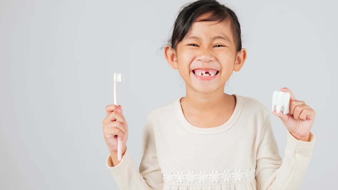 A young patient smiling at Locust Dental Group, holding a toothbrush and a model tooth
